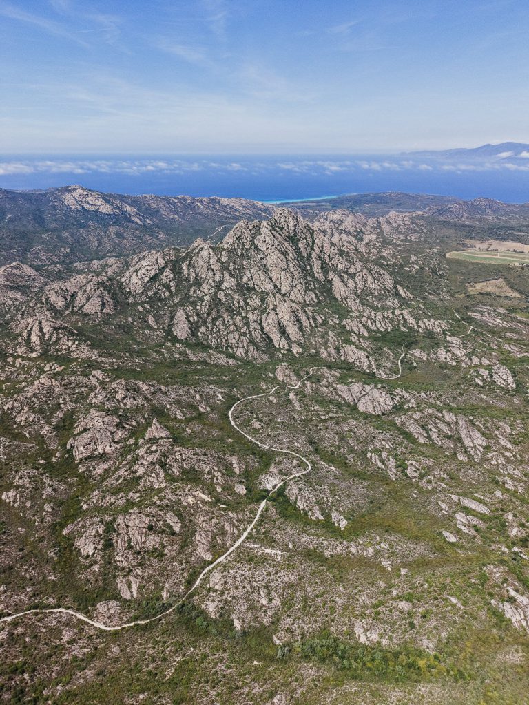 Curvas cerradas entre roca y maquis hasta el mar, desde el aire, sobre Córcega
