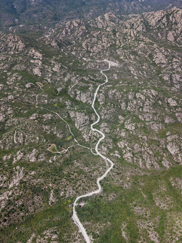 Estrechas curvas en S de una carretera clara en la montaña rocosa, desde el aire, en Córcega