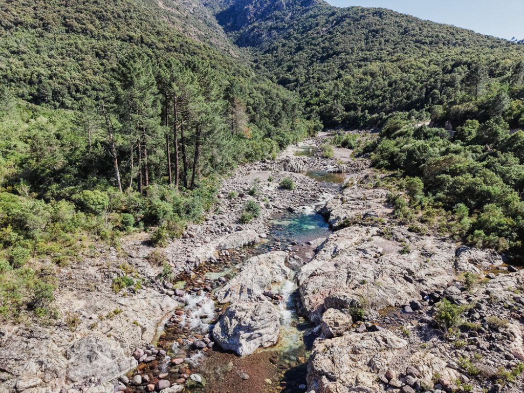 Pozas turquesas en el lecho pedregoso del río entre el bosque, desde el aire, en Córcega