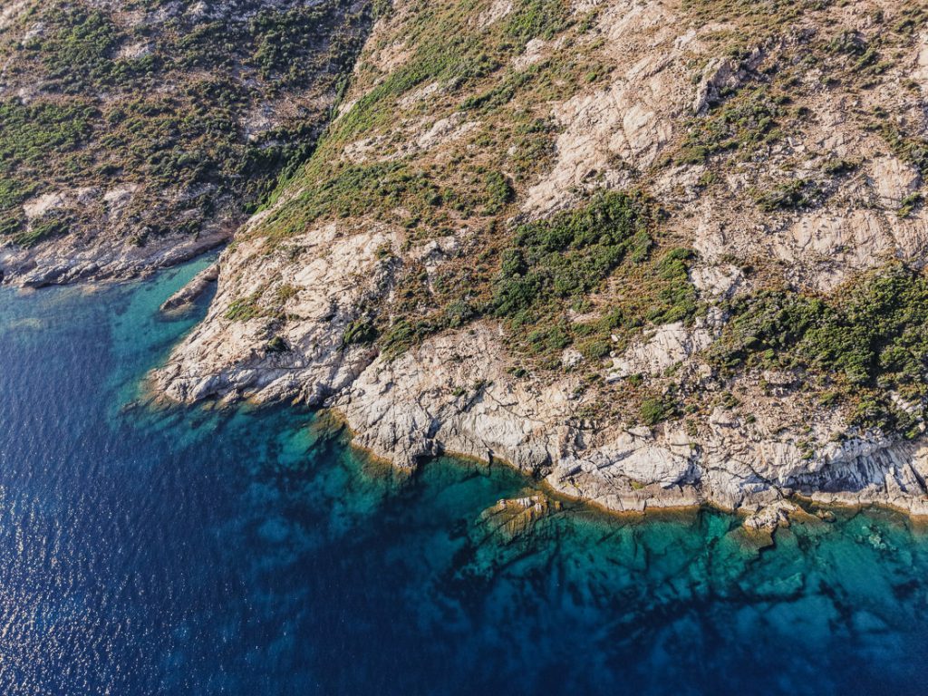 Roca clara y maquis sobre el agua cristalina, desde el aire, en la costa de Córcega