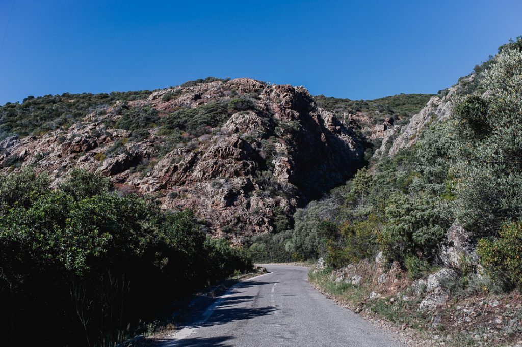 Curva de la carretera de montaña bajo una ladera rocosa con maquis en Córcega