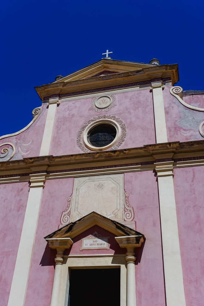 Fachada rosa de iglesia con rosetón e inscripción Dio vi salvi Regina, en Córcega
