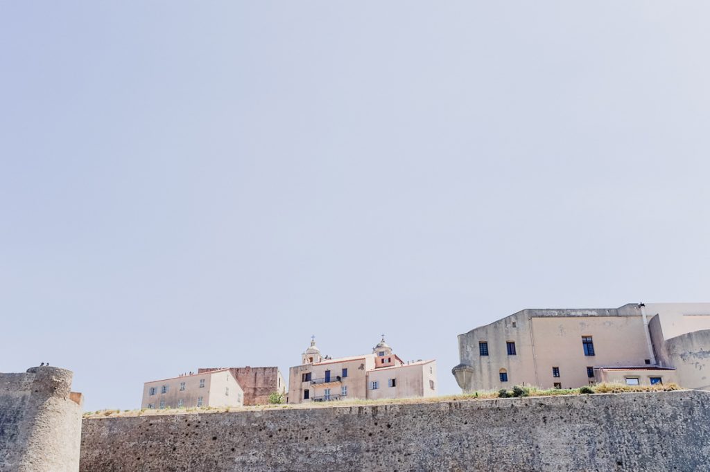 Casas y campanarios detrás de un muro alto, con mucho cielo encima en Córcega
