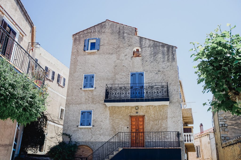 Casa con contraventanas azules, balcón de hierro forjado y escalera exterior en Córcega