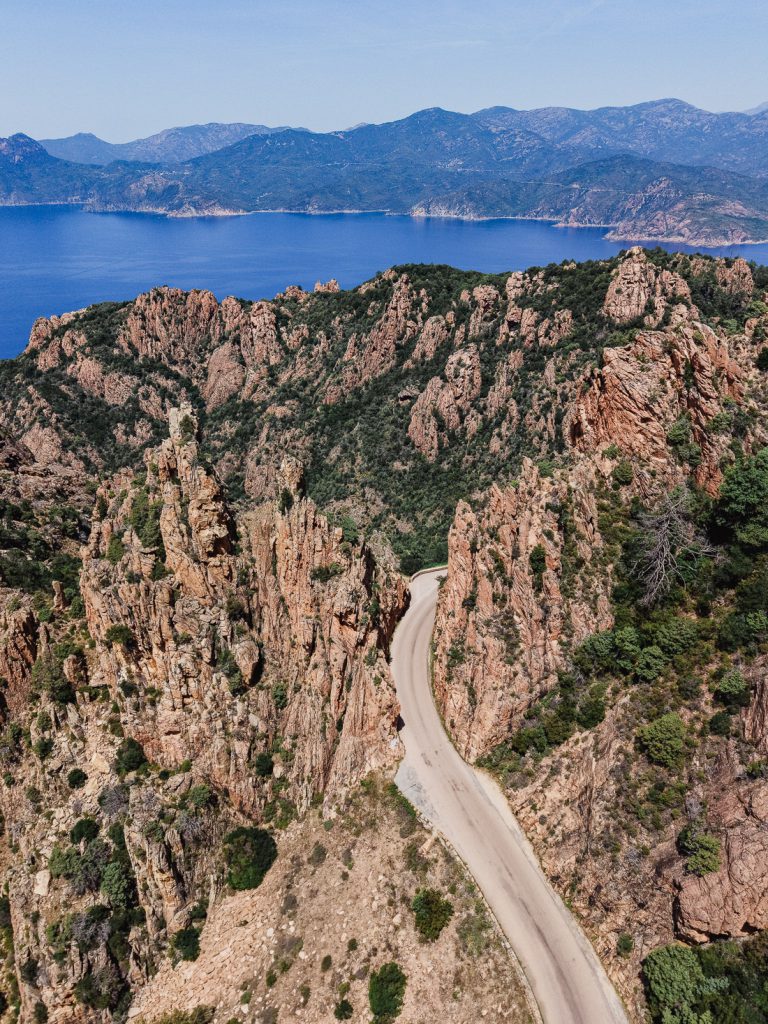 Curva cerrada entre paredes de roca roja de las Calanques, con el golfo detrás, desde el aire, en Córcega