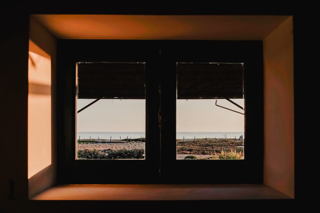 Vista a través de una ventana oscura hacia una valla, la playa y el mar en Córcega
