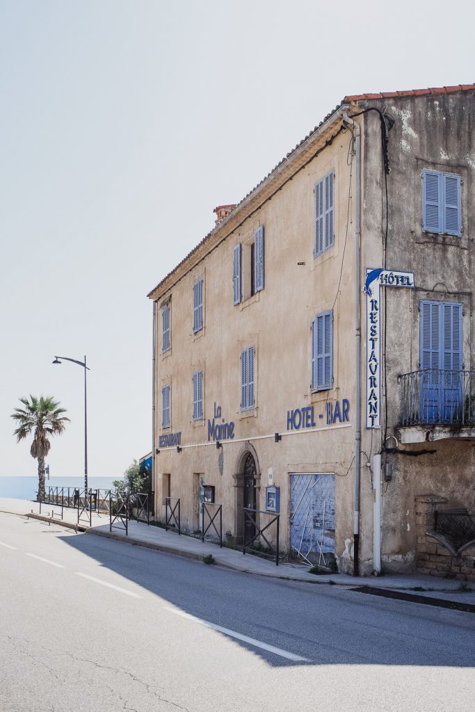 Casa descolorida con un letrero de Hotel-Bar en la carretera hacia el mar en Córcega