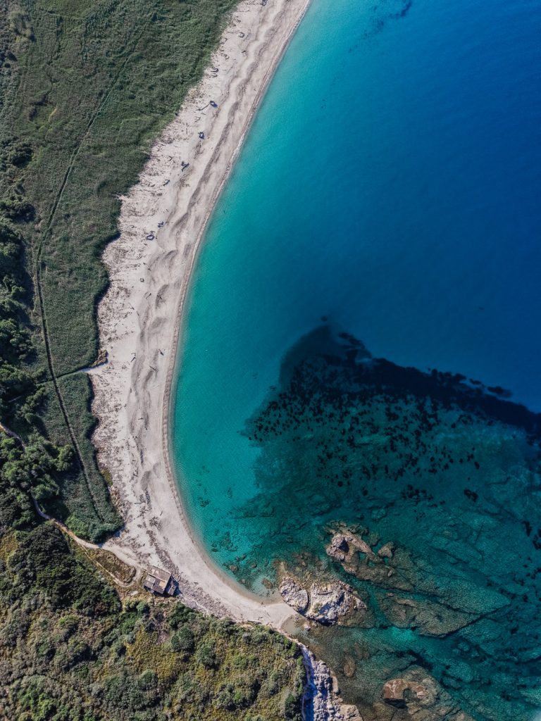 Curva de una playa, con manchas oscuras en el agua, desde el aire, en la costa de Córcega