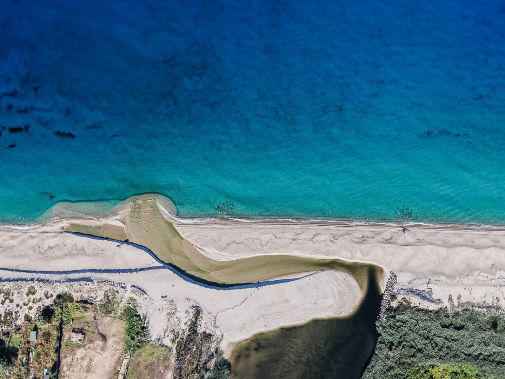 Arroyo que corre por la arena hasta el mar turquesa, desde el aire, en la costa de Córcega