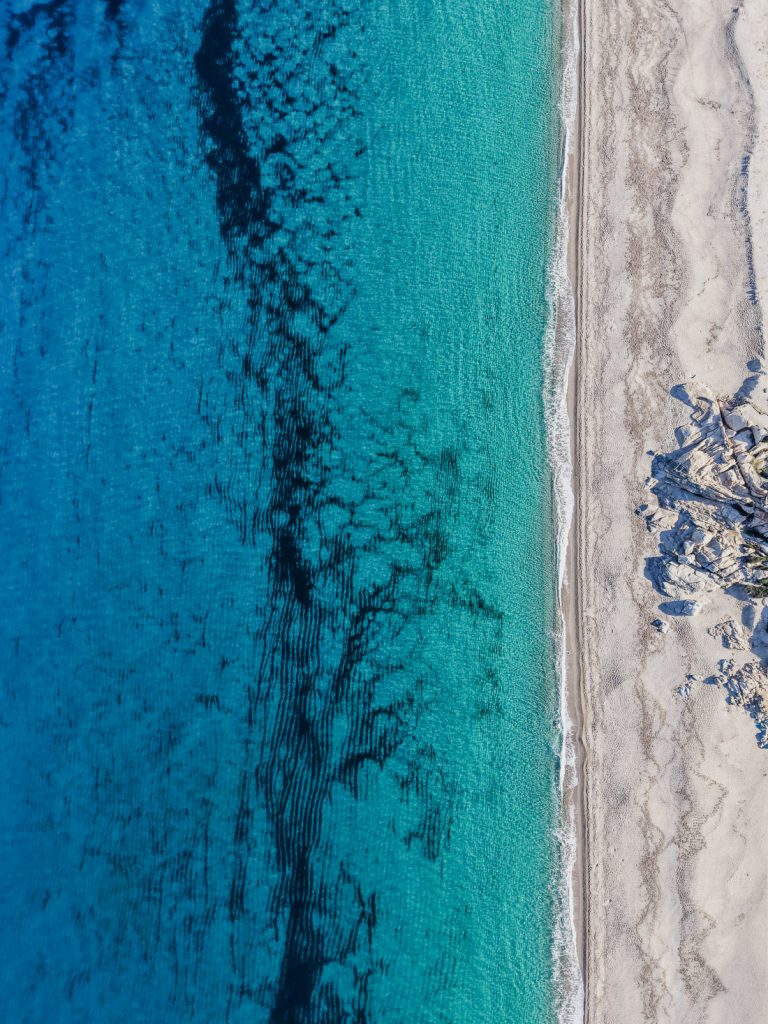 Agua clara con dibujos oscuros junto a la playa de arena, desde el aire, en Córcega