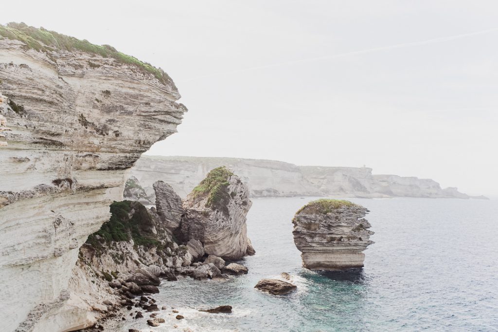 Acantilados de caliza estratificada y una roca en el mar cerca de Bonifacio en Córcega