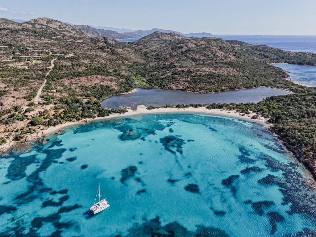 Un velero en el agua turquesa ante una laguna, desde el aire, en Córcega