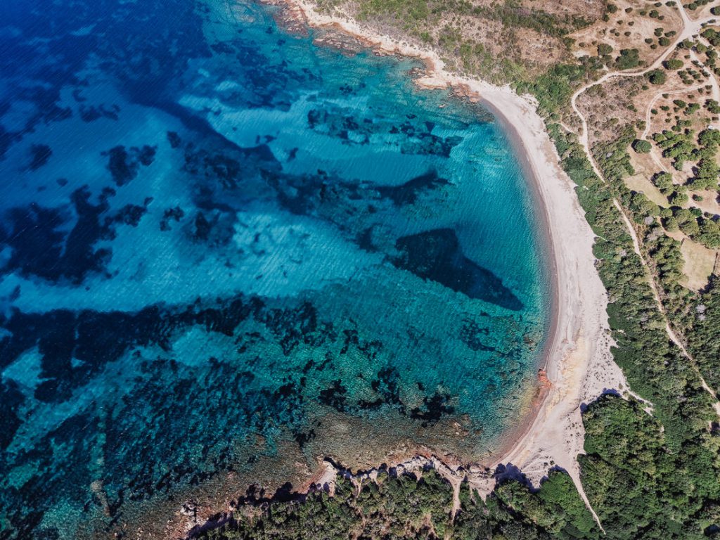 Curva de una playa de arena sobre fondo claro y oscuro, desde el aire, en Córcega