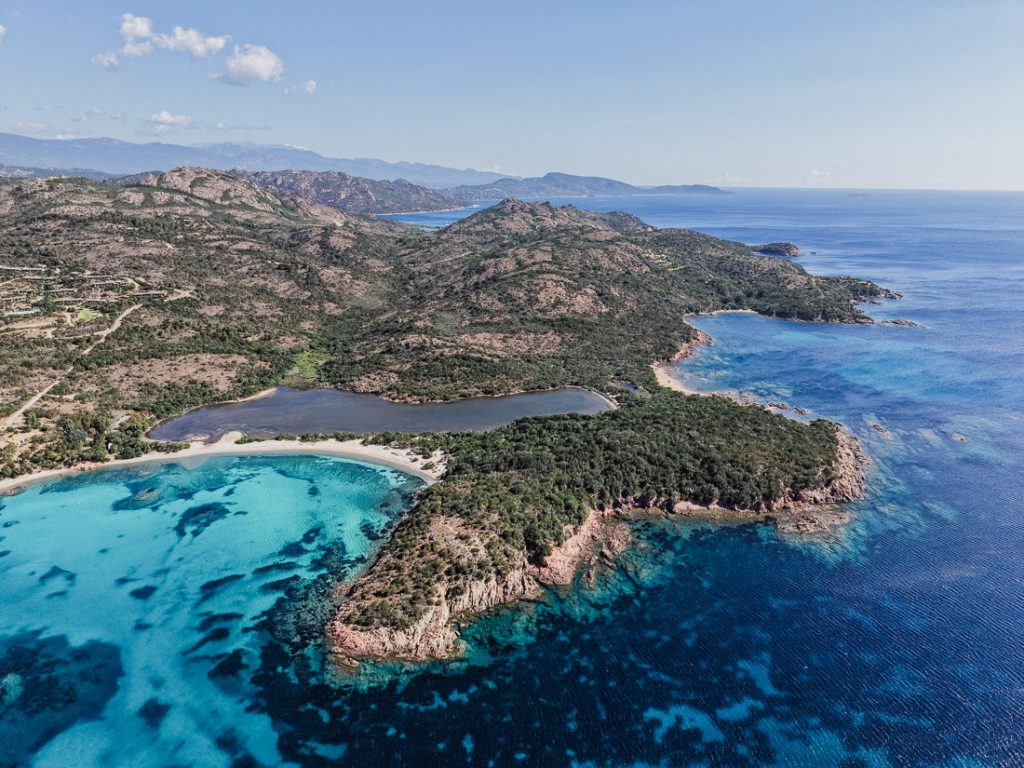Laguna, bahía turquesa y un promontorio boscoso, desde el aire, en Córcega