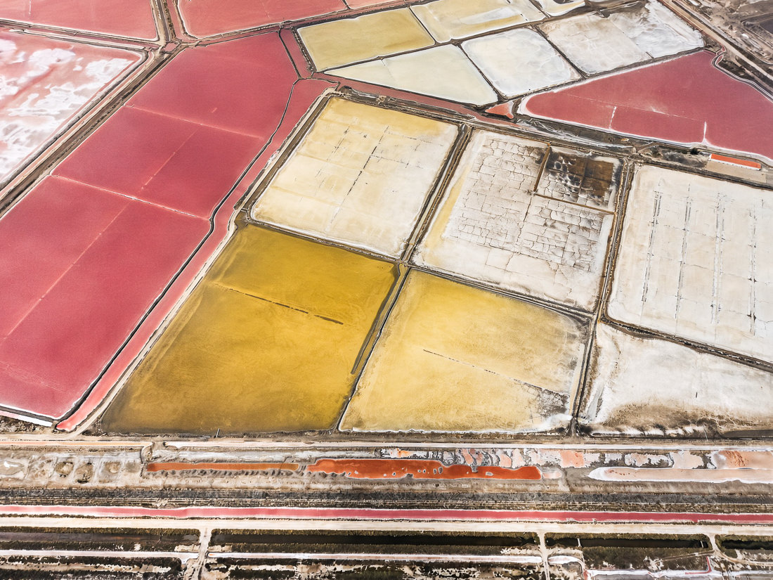 Rote, goldgelbe und weiße Salzbecken mit rissiger Kruste, unten schmale orange Kanäle, Provence